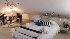 Une chambre à coucher avec un grand lit, deux fauteuils à rayures, une petite table avec une lampe et une branche décorative illuminée.