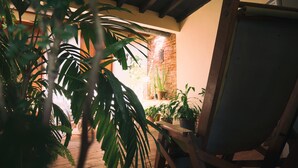 A wooden chair with a canvas backrest, a potted plant, and a brick wall in the background. - Casa Rogelio Inchauspi Bastida TRINIDAD (Trinidad)