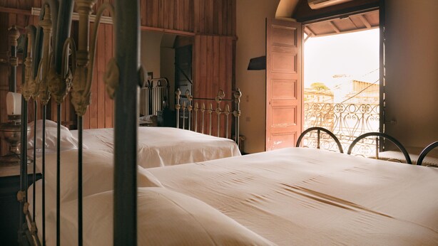 A room with two beds, wooden paneling, an open door leading outside, and a metal railing. - Casa Rogelio Inchauspi Bastida TRINIDAD (Trinidad)