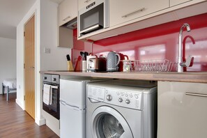 A compact kitchen with a microwave, oven, and washing machine. - (189OC-2) Minimalist Studio Near Beach & Town Centre  (Bournemouth)