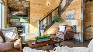 A cozy living room with a stone fireplace, a wooden staircase, and comfortable seating. - Heated Large Indoor POOL, VIEWS, Firepit, Location! 6BRCabin-sleeps 20 Game Room (Sevierville)