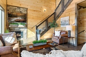 A cozy living room with a stone fireplace, a wooden staircase, and comfortable seating.