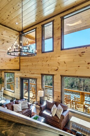 A spacious wooden cabin with multiple large windows, a cozy living area with a brown leather sofa, and a hanging light fixture.