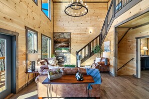 Cozy seating area with a leather sofa, armchair, and coffee table, surrounded by a stone fireplace and staircase.