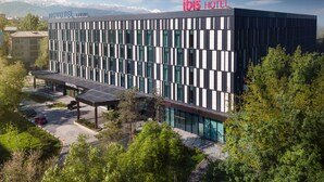 A modern hotel with a flat roof, large windows, and a parking area. - Novotel Living Almaty Jetisu (Almaty)
