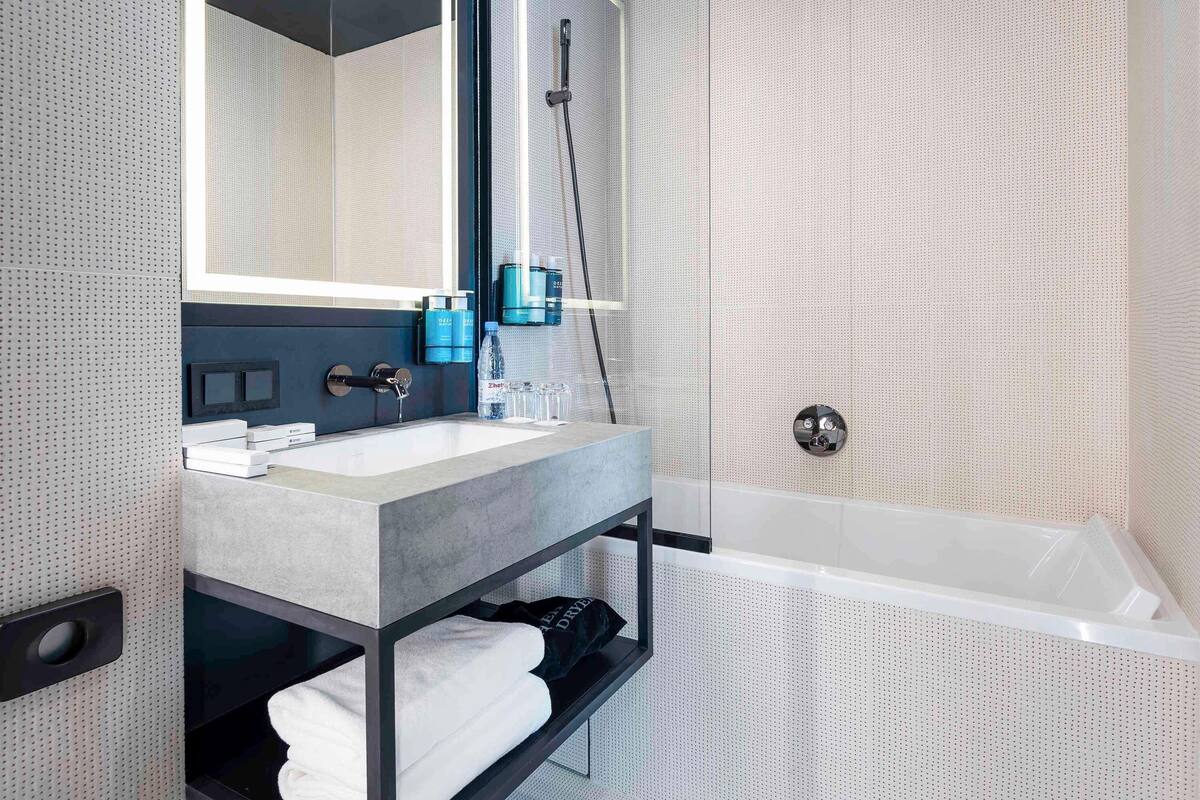 Un baño moderno con un espejo grande, una bañera y un tocador con lavabo y espacio para almacenamiento.