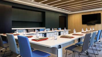 A conference room with a long table, chairs, water bottles, glasses, and a flat-screen TV on the wall.