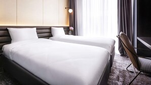 A hotel room with two beds, a nightstand, a lamp, and a chair. - Novotel Living Almaty Jetisu (Almaty)