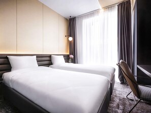 A hotel room with two beds, a nightstand, a lamp, and a chair. - Novotel Living Almaty Jetisu (Almaty)
