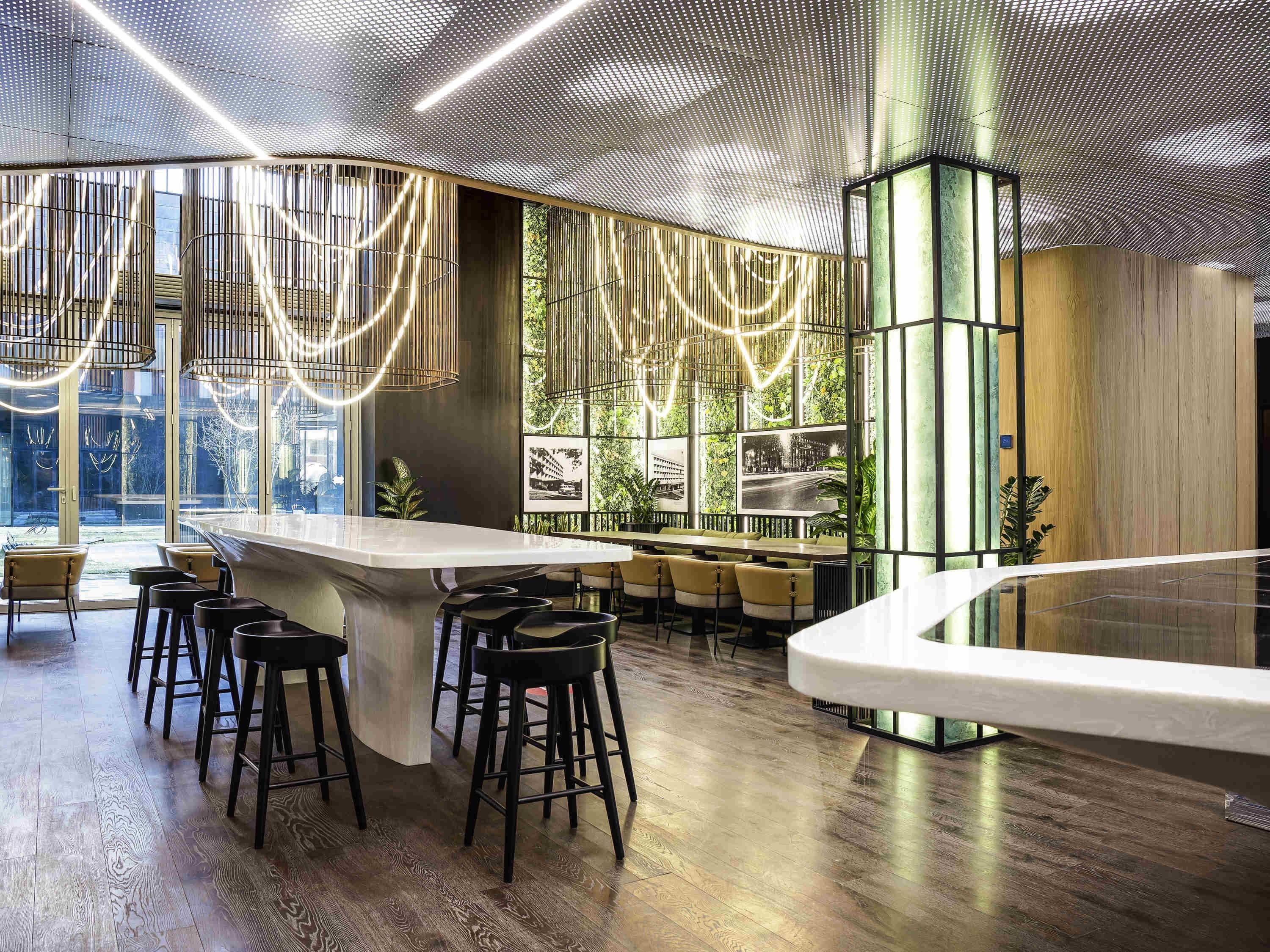 Uma área de bar moderna com balcão curvo, banquetas pretas e teto com padrão perfurado.
