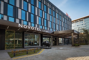 A modern hotel exterior with a large glass facade, a prominent entrance, and a bull sculpture in front. - Novotel Living Almaty Jetisu (Almaty)