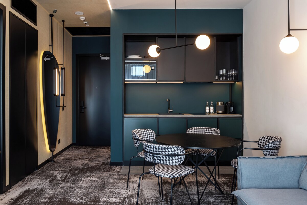 A modern kitchen with a round dining table, houndstooth chairs, and pendant lighting.