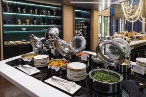 A buffet setup with various food stations, including a salad bar, hot dishes, and a beverage area. - Novotel Living Almaty Jetisu (Almaty)