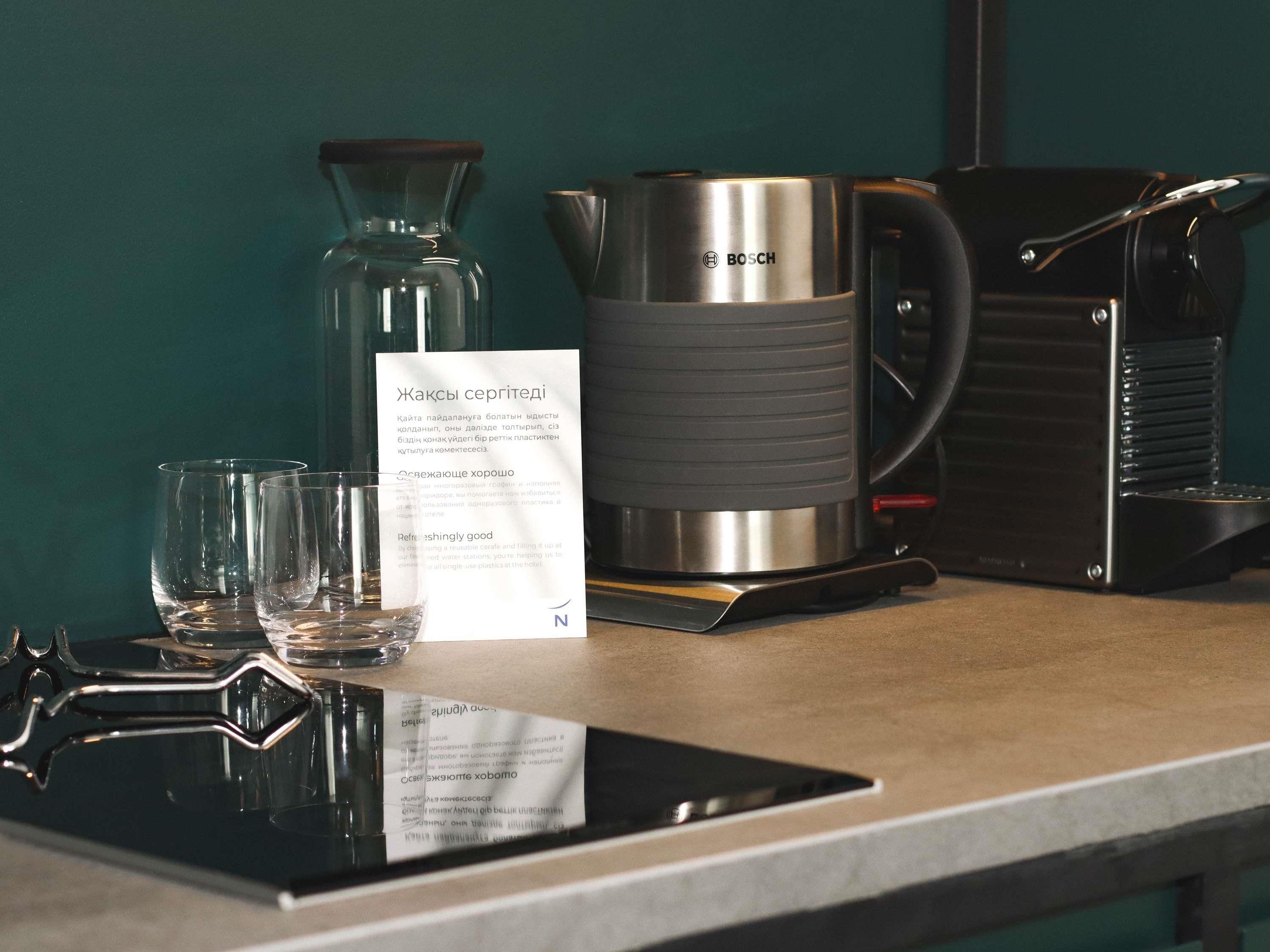 A coffee maker, a glass carafe, and a glass on a table with a menu.