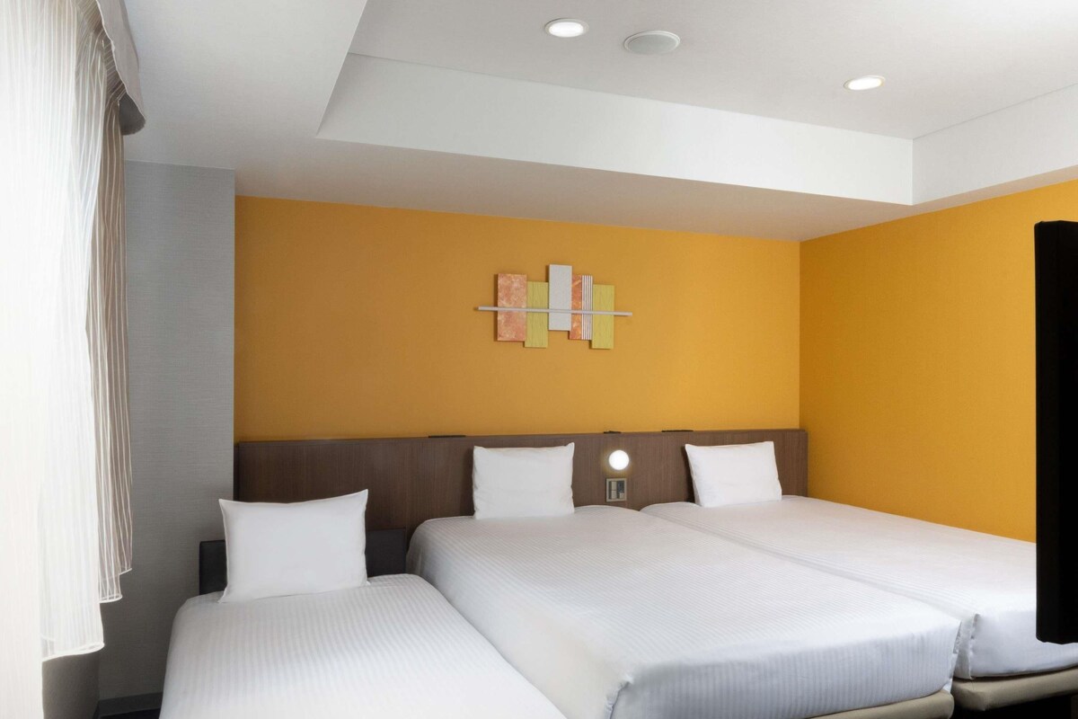A hotel room with two beds, a modern light fixture, and a wall art piece.