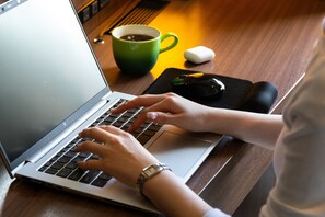 A laptop on a wooden table with a green mug and a black mouse. - Ibis Styles Kyoto Shijo (Kyoto)