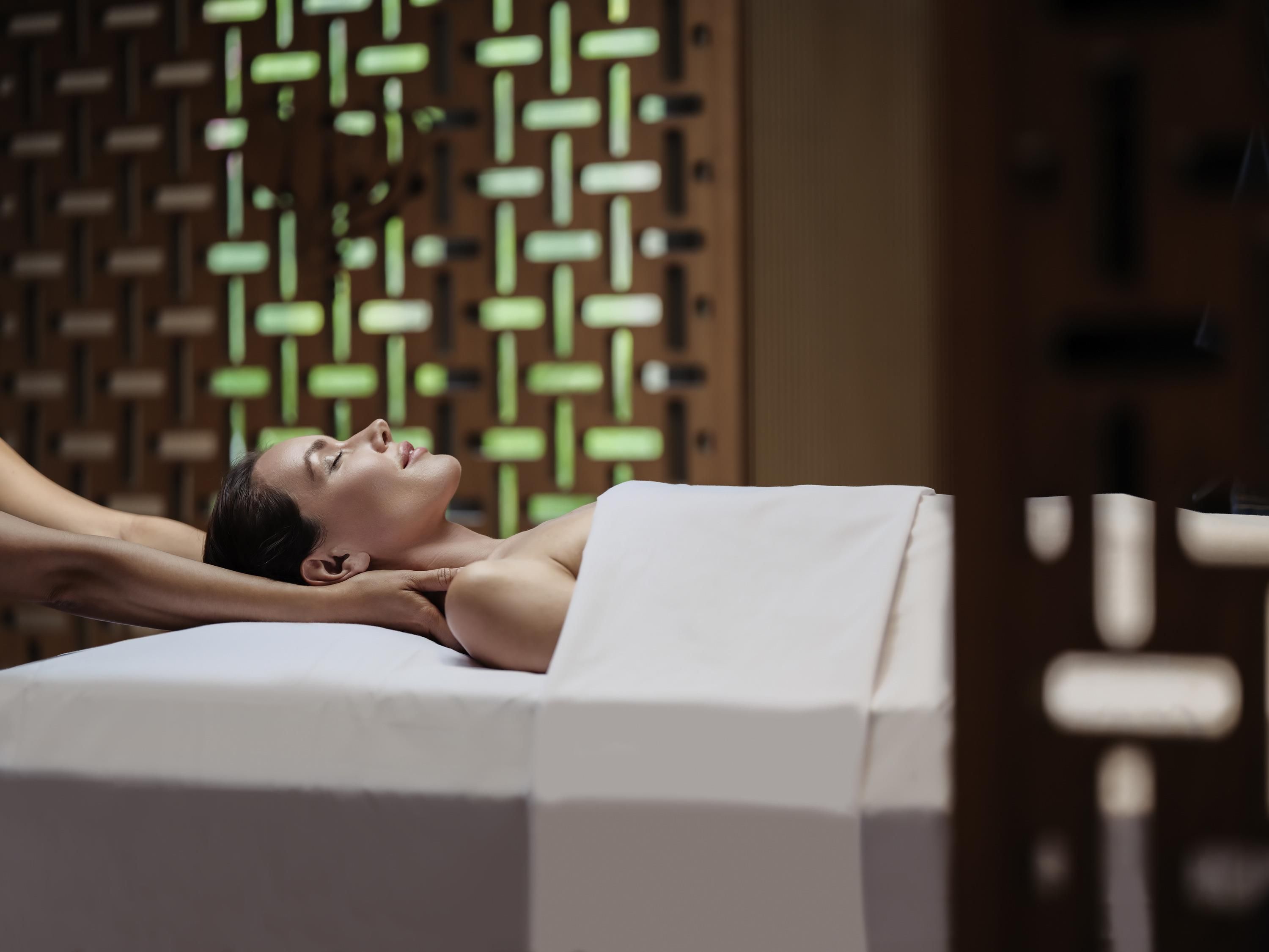 A person lying on a massage table in a room with a patterned wall.