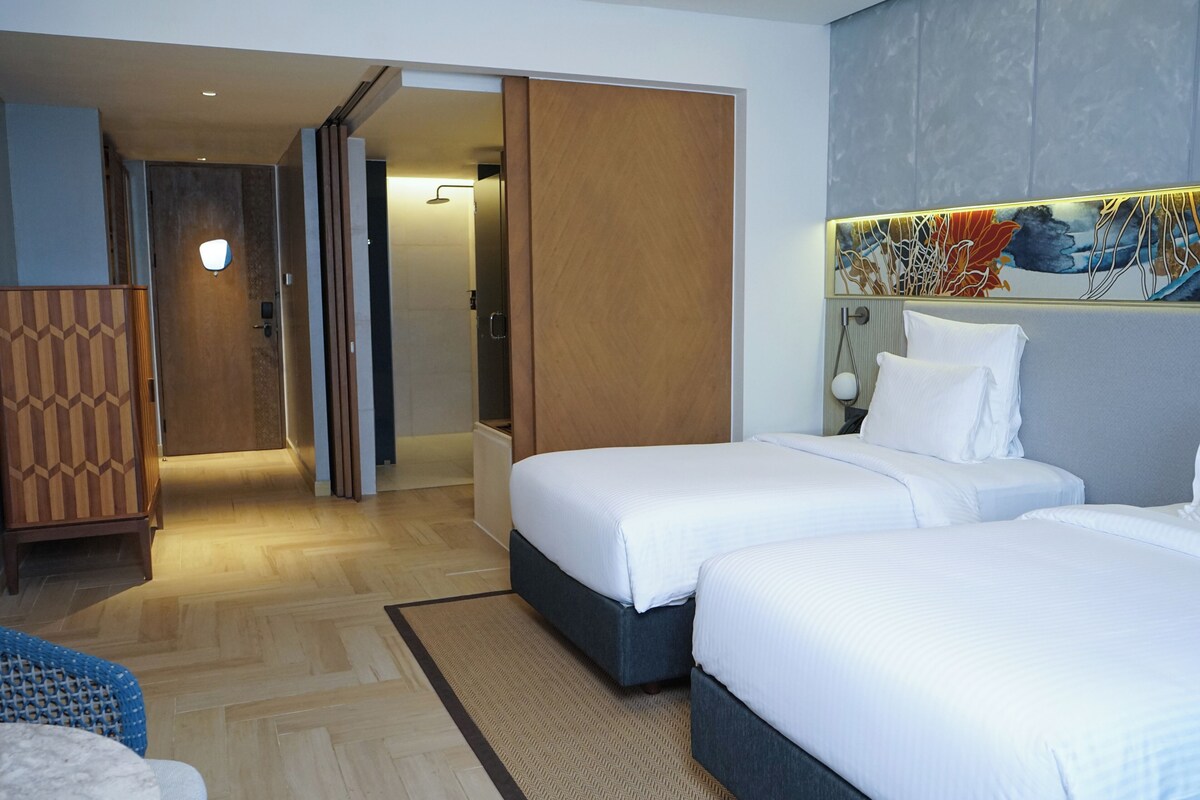 Hotelkamer met twee bedden, een houten garderobe, een badkamer met douche en een groot abstract schilderij aan de muur.