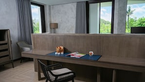 Une pièce moderne avec un grand bureau en bois, une chaise en osier noire, une lampe et une vue sur la verdure grâce à de grandes fenêtres.