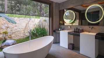 Un baño moderno con una bañera independiente, dos lavamanos y un espejo grande con marco circular.