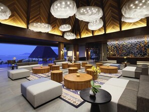 Eine moderne Lobby mit runden Holztischen, gepolsterten Sitzgelegenheiten und einem großen Fenster mit Blick auf ein Gewässer.