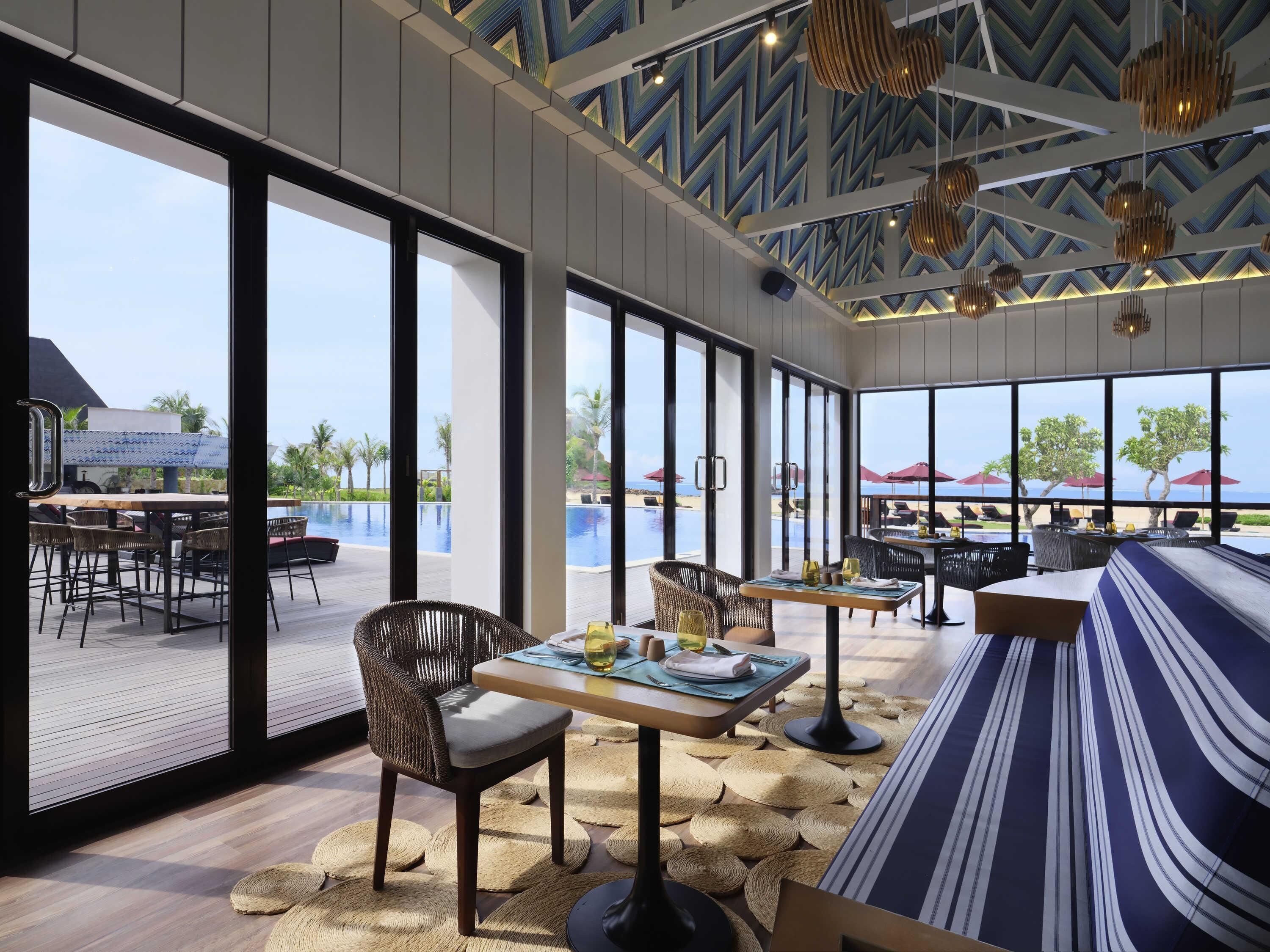 A modern outdoor dining area with large windows, wicker furniture, and a pool view.