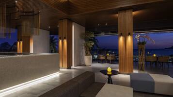 A modern indoor space with wooden beams, seating areas, and a view of the ocean.