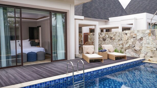 Une chambre d’hôtel moderne dotée d’une grande porte-fenêtre coulissante donnant sur un balcon avec piscine.