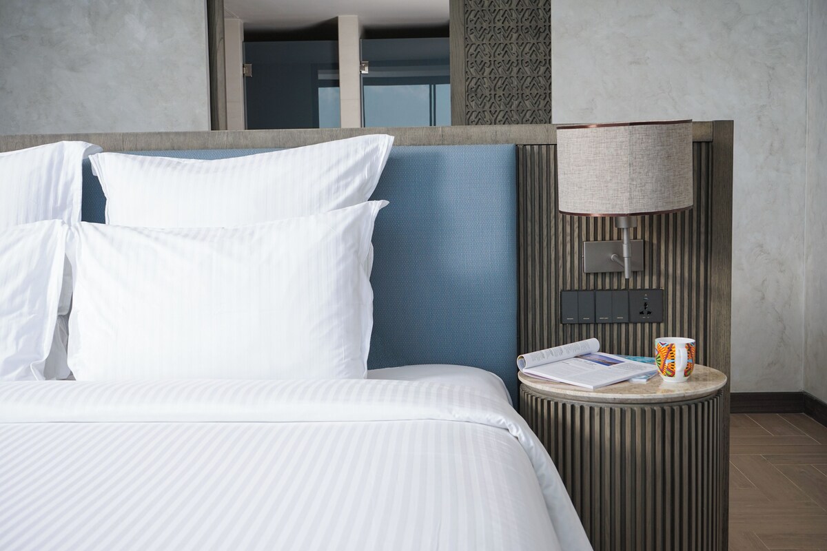 Hotelkamer met een bed, kussens, een nachtkastje met een lamp, een mok en een boek.