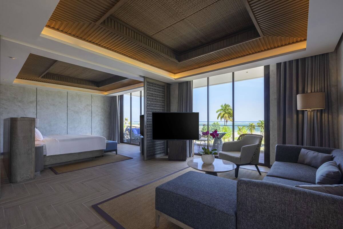 Une chambre d’hôtel moderne équipée d’un lit, d’un canapé, d’une télévision et offrant une vue sur l’océan.