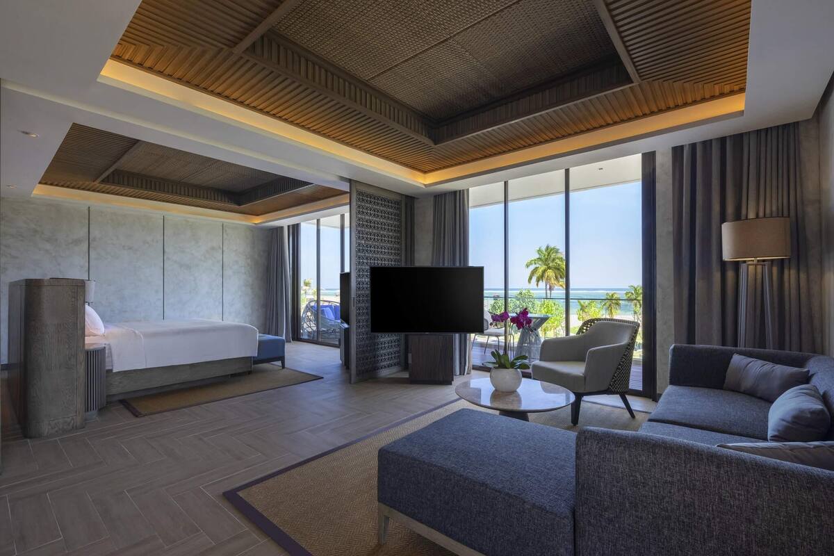 A modern hotel room with a bed, sofa, TV, and a balcony with a view.