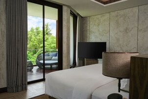 Ein Hotelzimmer mit einem großen Bett, einem Fernseher, einer Lampe und einem Balkon mit Korbsessel und Blick ins Grüne.