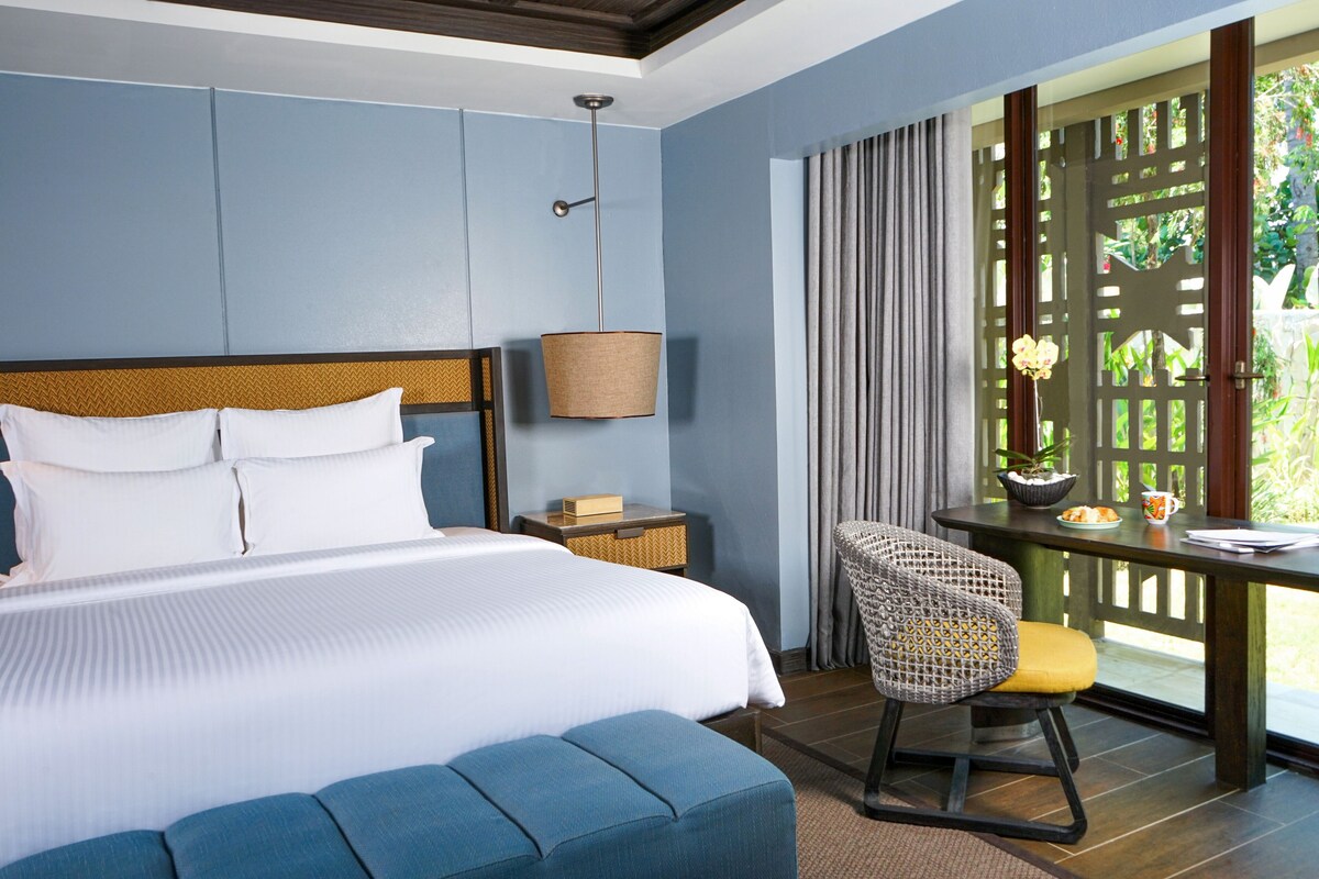 Hotelkamer met een groot bed, een bureau met stoel, een lamp en uitzicht door een houten latticestoel.