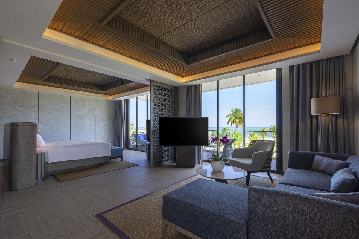 Une chambre d’hôtel moderne équipée d’un lit, d’un canapé, d’une télévision et offrant une vue sur l’océan.