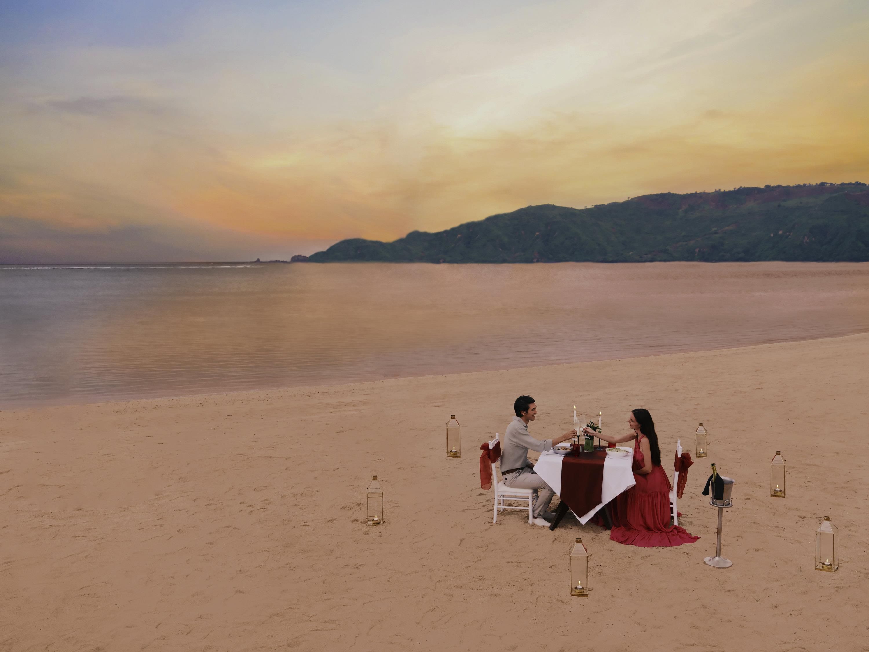 A beachside table set for two with a view of the sea and distant hills.