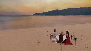 A beachside table set for two with a view of the sea and distant hills.