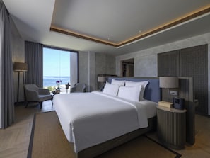 A modern hotel room with a large bed, a seating area with a view of the ocean, and a small table with a lamp. - Pullman Lombok Merujani Mandalika Beach Resort  (Kuta)