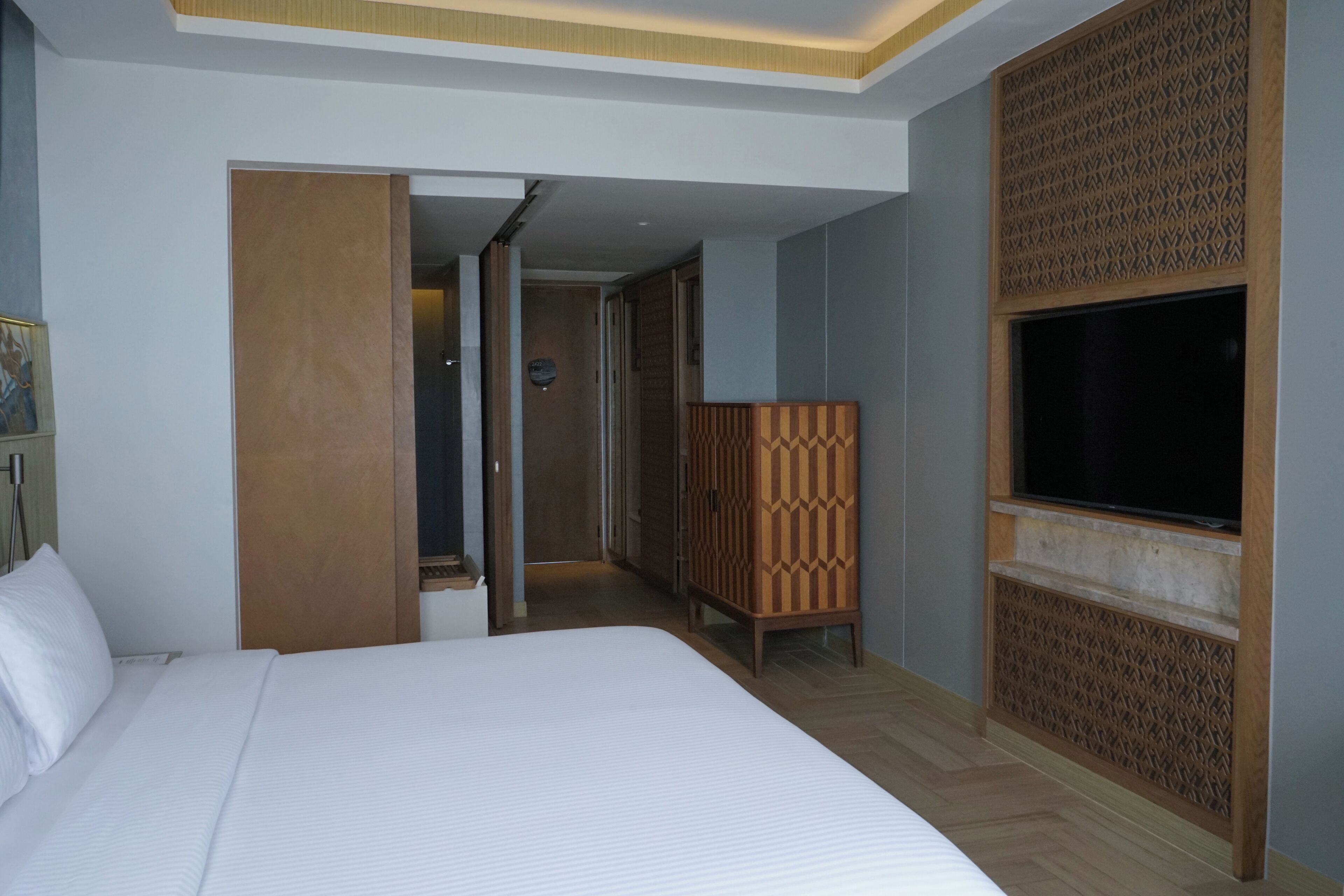 A hotel room with a large bed, a TV mounted on the wall, and a wooden partition.