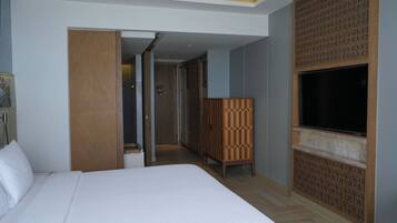 A hotel room with a large bed, a TV mounted on the wall, and a wooden partition.
