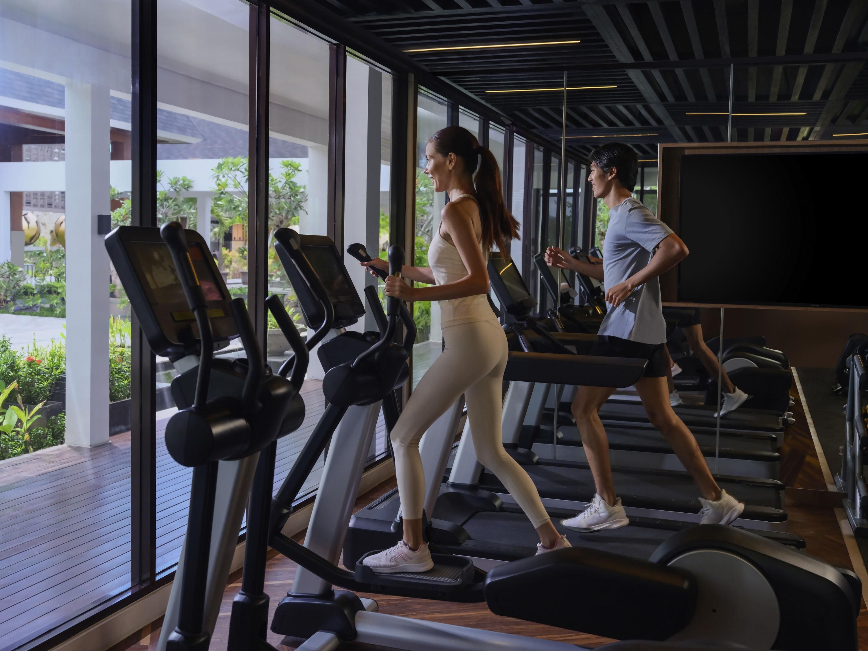 A gym with treadmills, large windows, and a view of greenery outside.