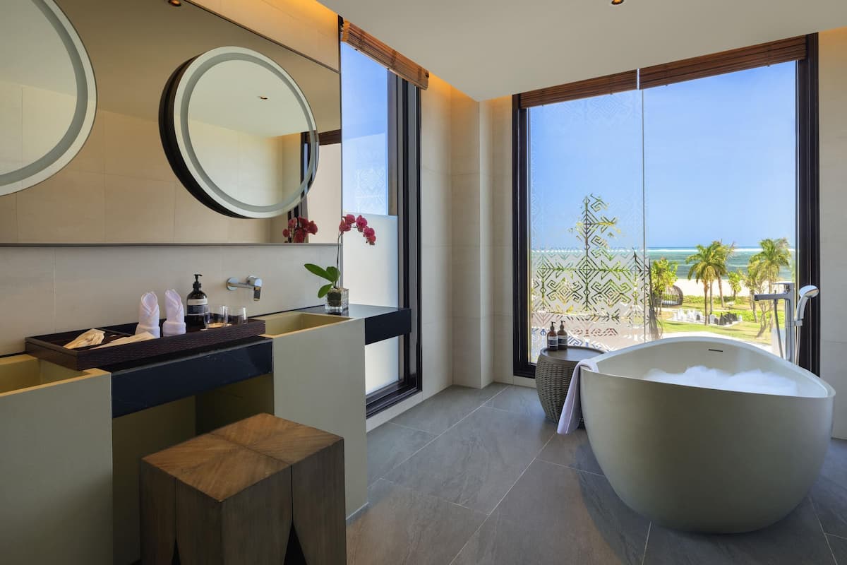 A modern bathroom with a large bathtub, a vanity with a mirror, and a view of the ocean.