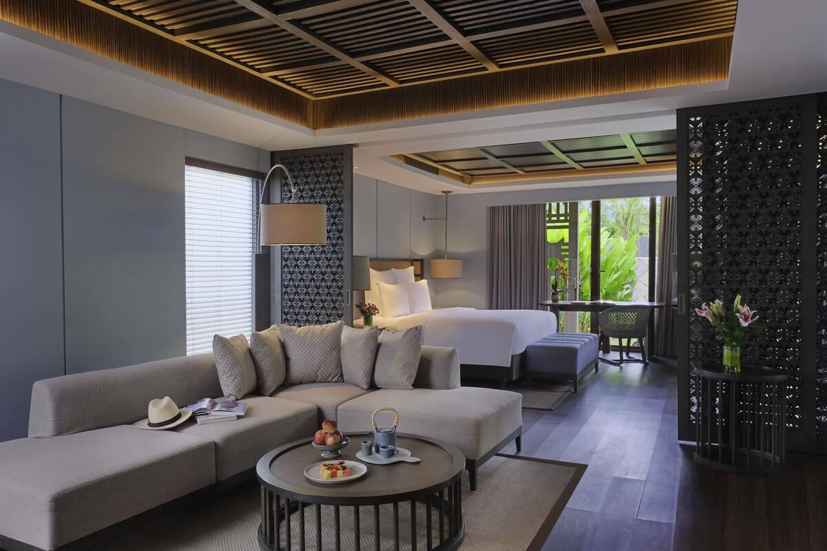 Une chambre d’hôtel moderne, dotée d’un canapé, d’une table basse ronde, d’un lit et d’un balcon offrant une vue sur la verdure.