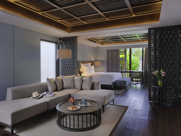 Ein modernes Hotelzimmer mit einer Couch, einem runden Couchtisch, einem Bett und einem Balkon mit Blick auf Grünflächen.