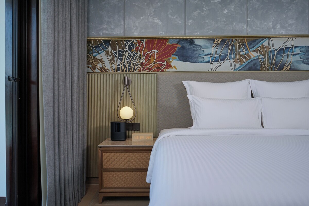 Hotelkamer met een bed, nachtkastje met lamp, klok en decoratief paneel.