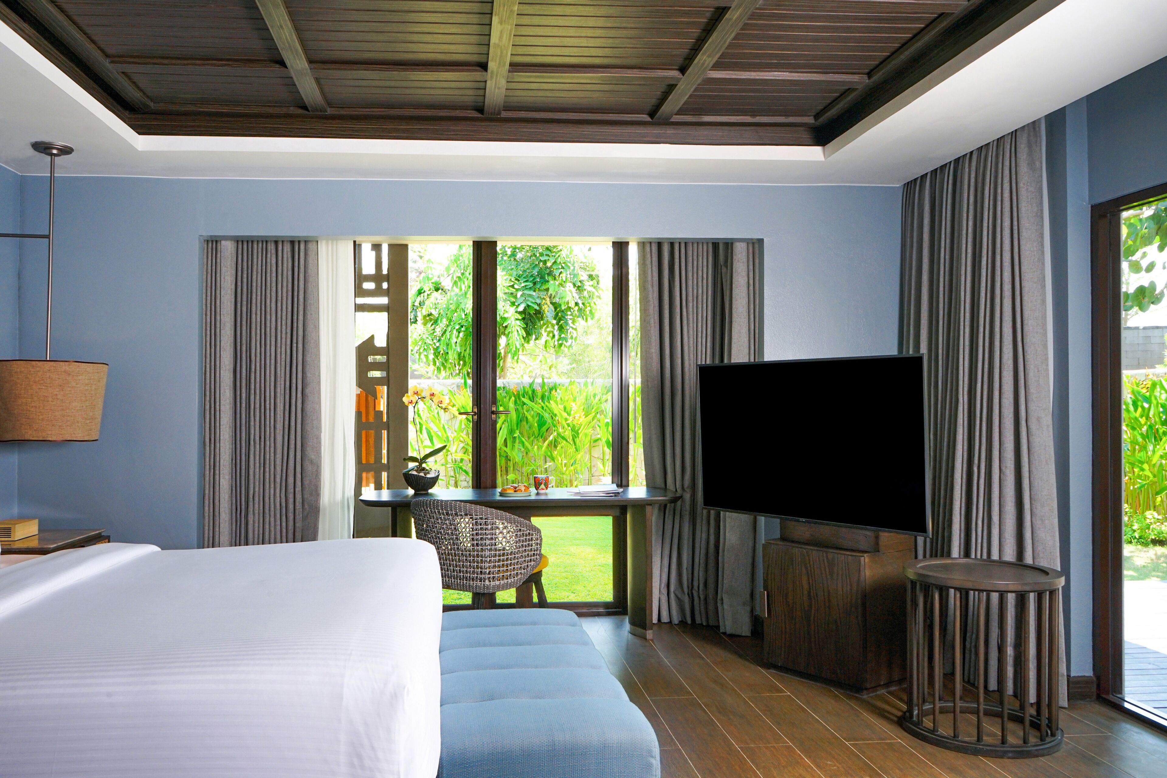 A hotel room with a bed, a TV, a small table with a chair, and a window with curtains.