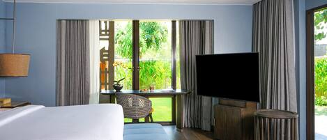 A hotel room with a bed, a TV, a small table with a chair, and a window with curtains.