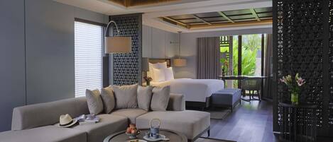 A modern hotel room with a sofa, a round coffee table, a bed, and a balcony with a view of greenery.