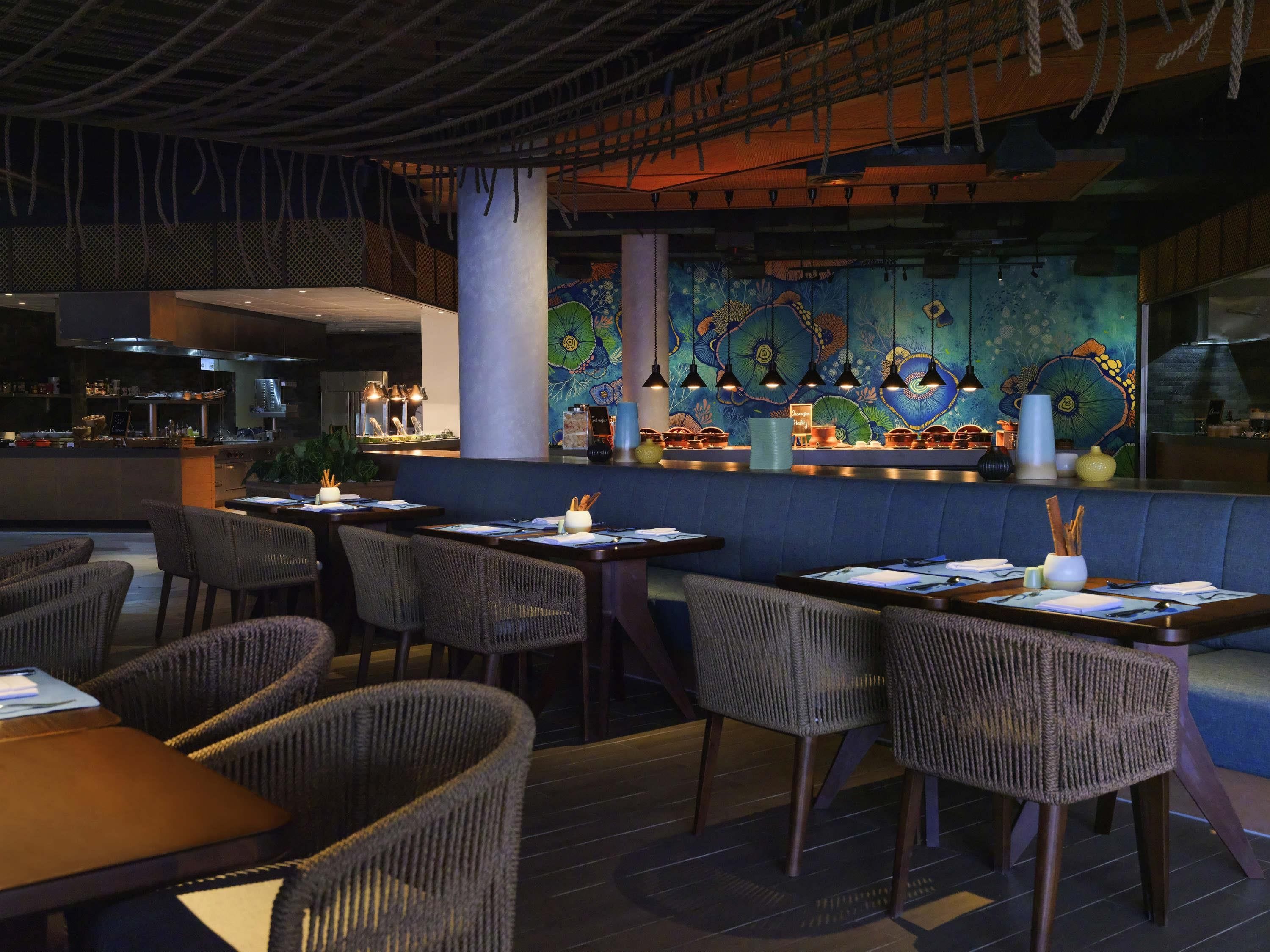 A restaurant with wicker chairs, a bar area, and a mural.