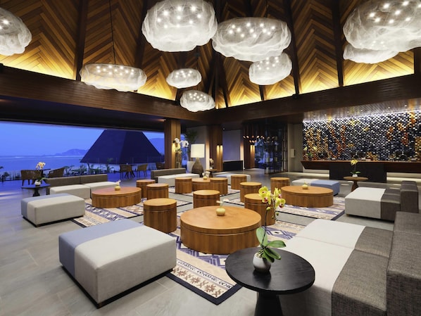 Un hall d’entrée moderne avec des tables rondes en bois, des sièges confortables et une grande fenêtre donnant sur un plan d’eau.