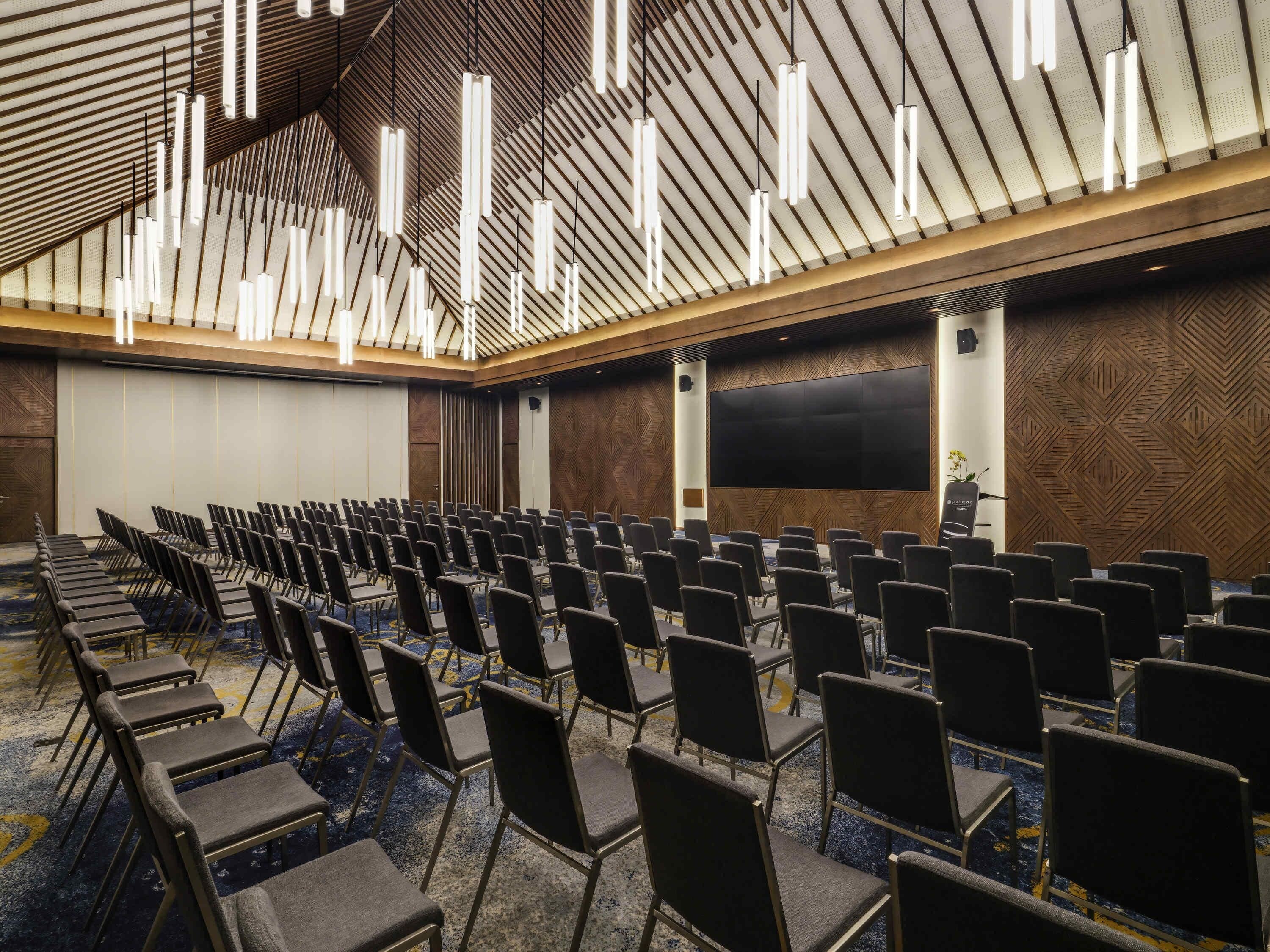 A conference room with rows of chairs, a large screen, and modern lighting fixtures.